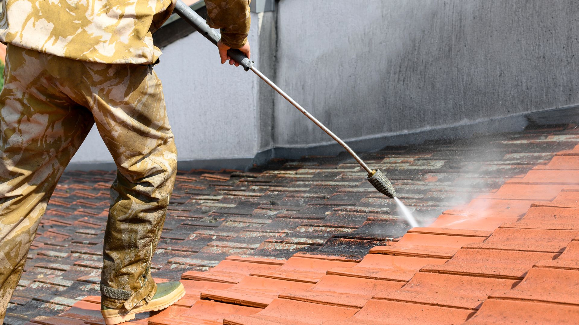 Worker using high-pressure washer to clean terracotta tile roof surface