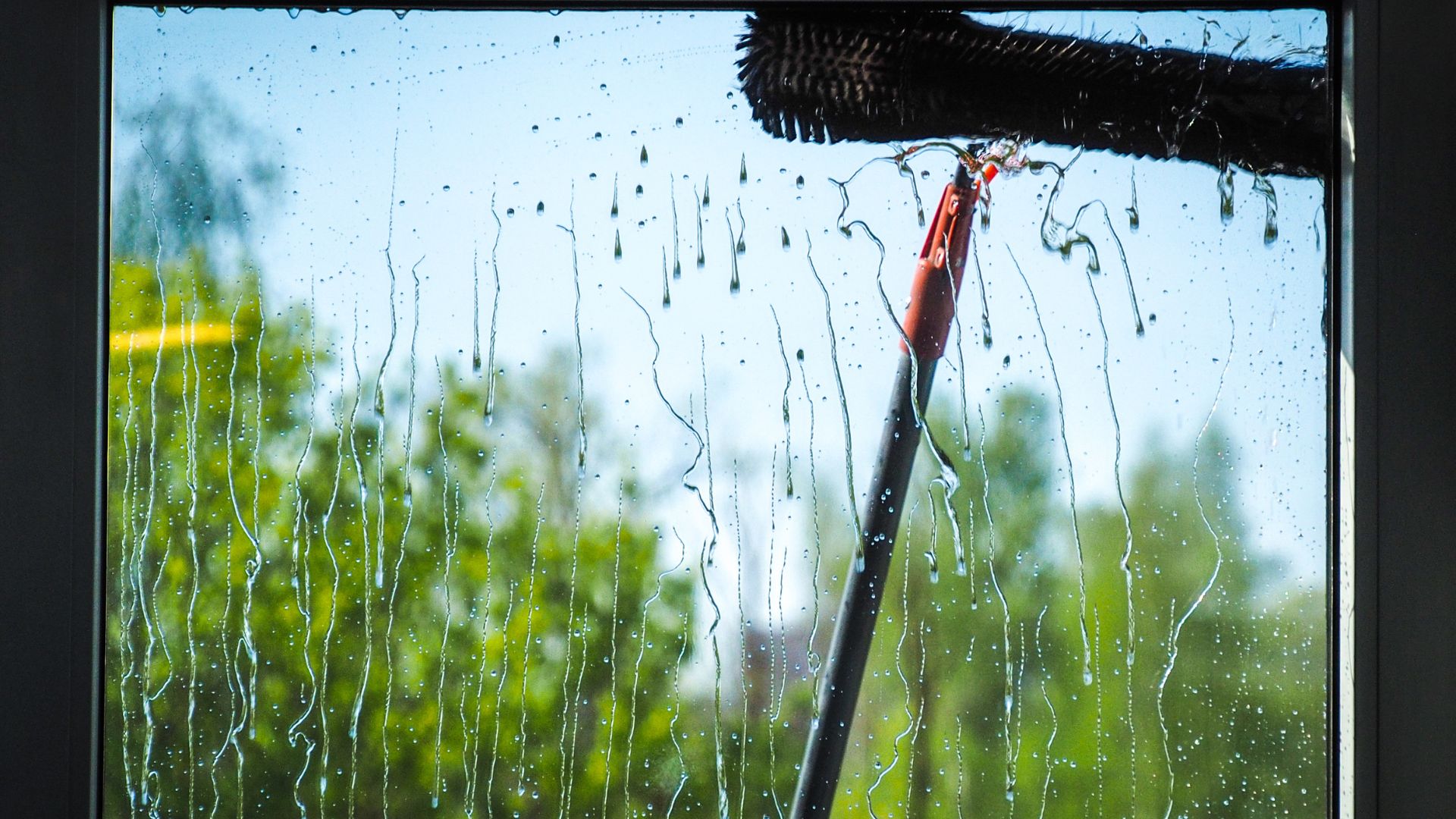 Rainy window with windshield wiper clearing water droplets on glass