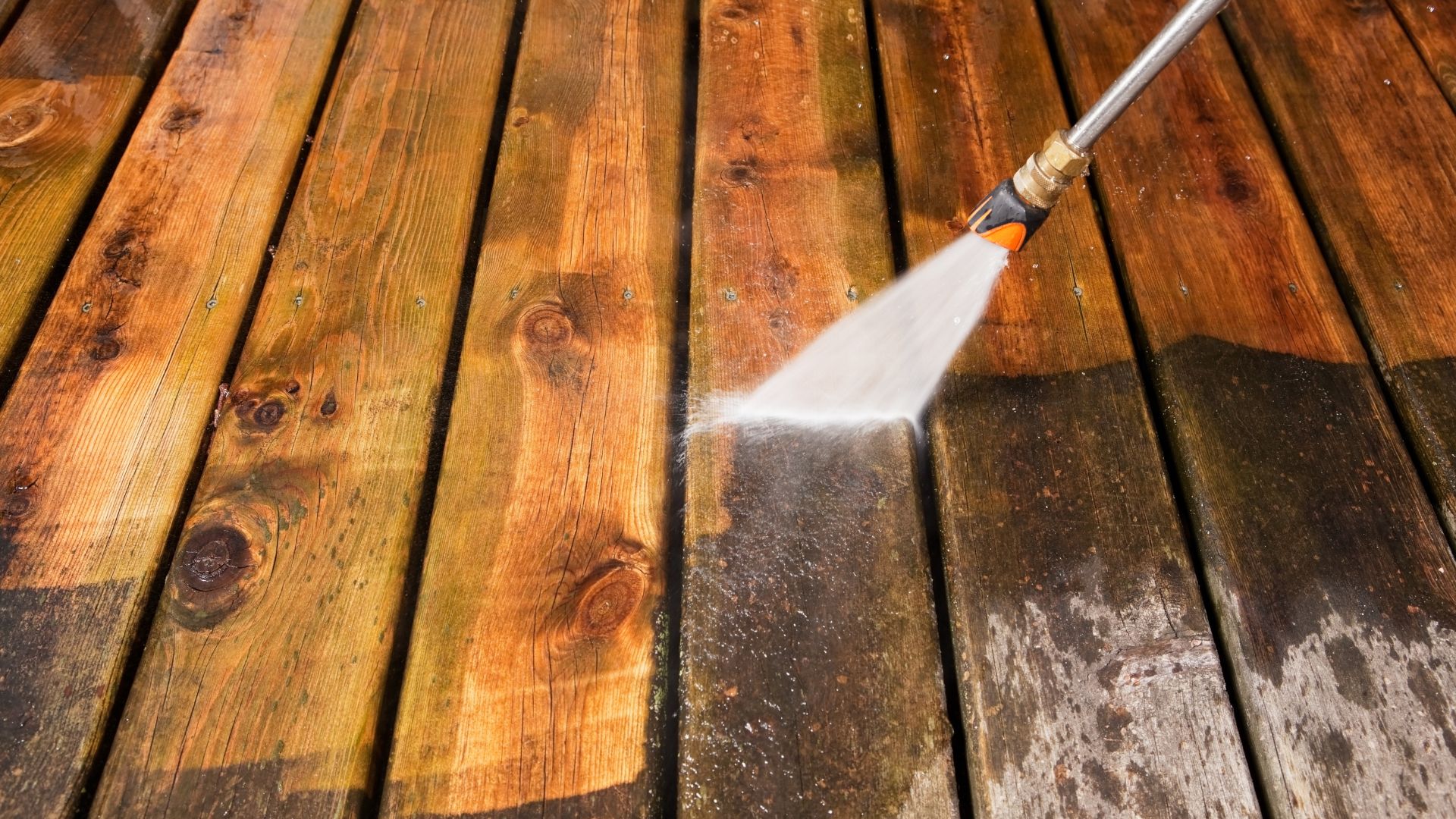 Pressure washer cleaning wooden deck, revealing clean and dirty surfaces