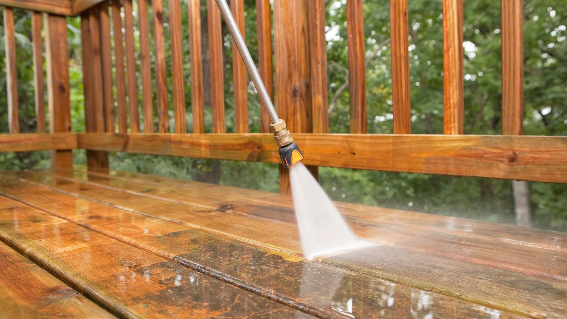 Pressure washer cleaning wooden deck with spray of water